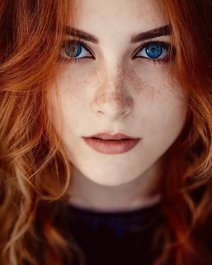 Portrait d'une jeune femme aux cheveux roux et yeux bleus, regard intense.