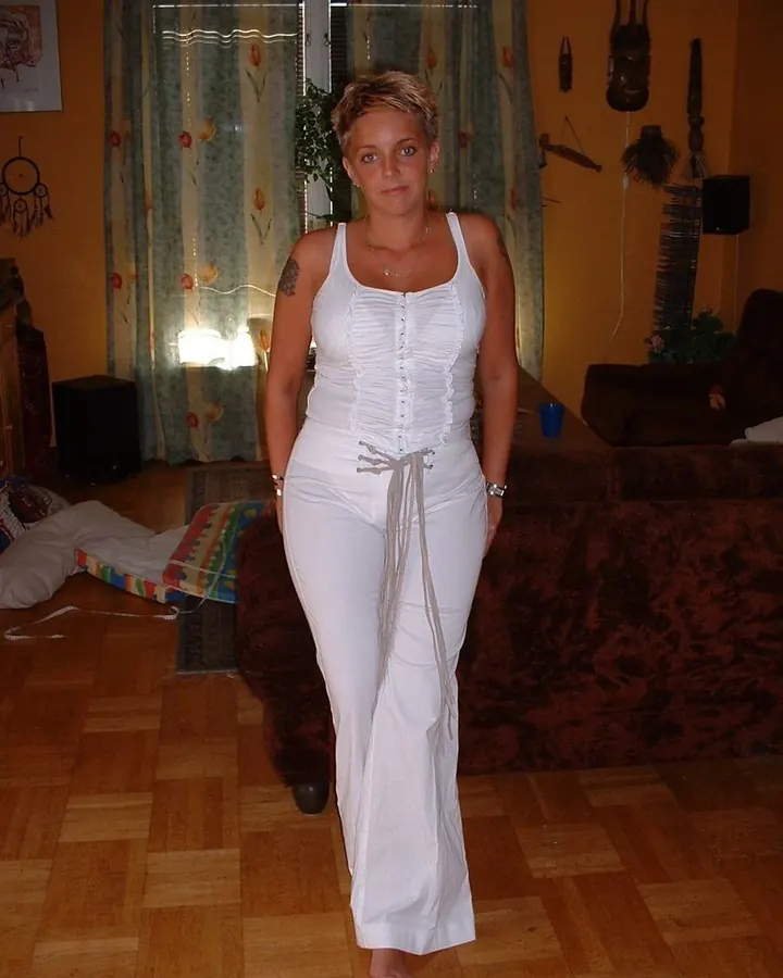 Femme aux cheveux courts blonds en tenue blanche dans un salon coloré.